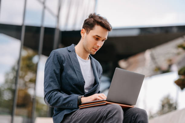 istock Concentrated young man is typing on his laptop while sitting outdoors. 1997852122
