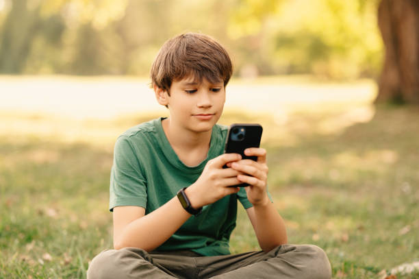 istock Serious handsome teen boy is browsing his phone while sitting in a park. 1997854289