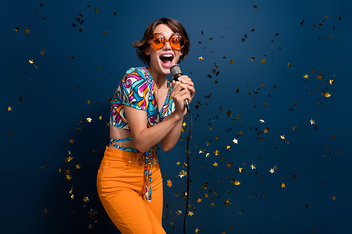 Photo portrait of lovely young lady singing mic party energetic wear trendy flared pants garment isolated on dark blue color background.
