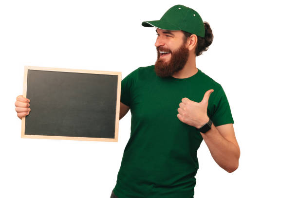 istock Handsome bearded man in green is holding an empty blackboard and thumb up. 1997863894
