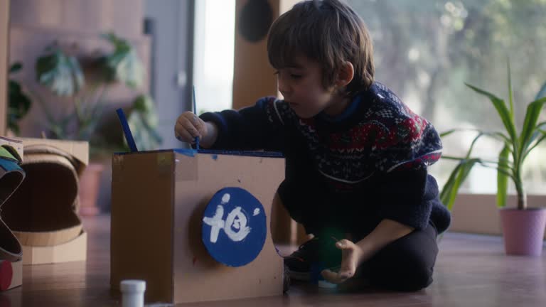 Little child boy painting his space helmet mad of cardboard.