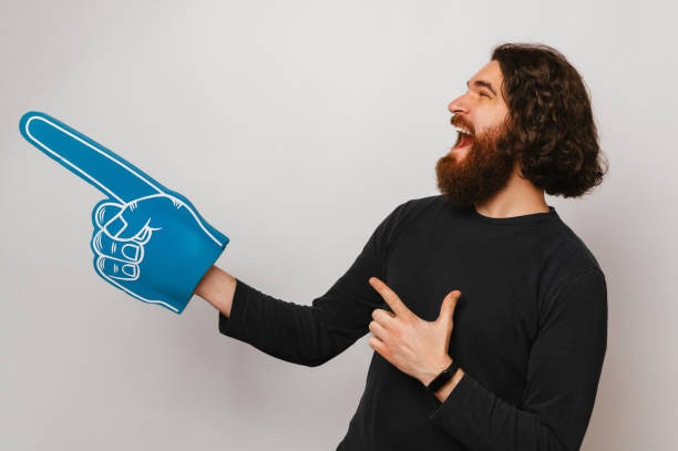 istock Ecstatic long hair bearded man wearing fan foam finger glove points aside. 1997875780