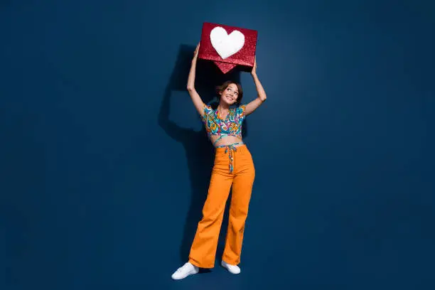 Photo of Full size photo of attractive young woman hold look heart icon notification wear trendy flared pants isolated on dark blue color background