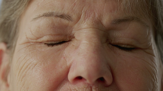 Senior woman closing eyes in contemplation in macro close-up. Eye_s detail of an older lady with wrinkles of wisdom in meditation. Person opening eyes and smiling