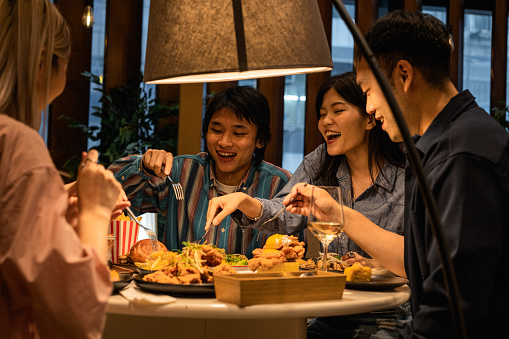 Group of young Asian friends delighting in their meal, taking bites at a restaurant