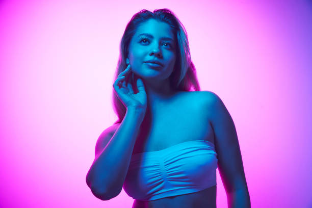 istock Tender, attractive young woman wearing white top, posing against gradient studio background in neon light. Health and wellness 1997904257