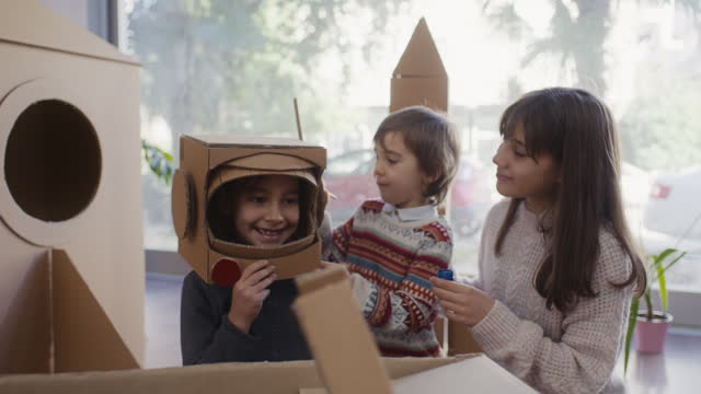 Children doing home activity at home, they are painting their astronaut helmets made of cardboard.