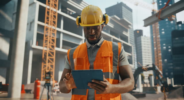 Portrait of a Handsome Black Civil Engineer Working on a Tablet at a Construction Site. Young African Man Standing Outdoors, Using Computer Device for Planning and Developing a Real Estate Project