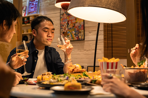 At a restaurant, two young Asian men are depicted happily taking bites of their food