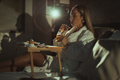 A young woman wearing a bathrobe having breakfast in bed in a hotel room