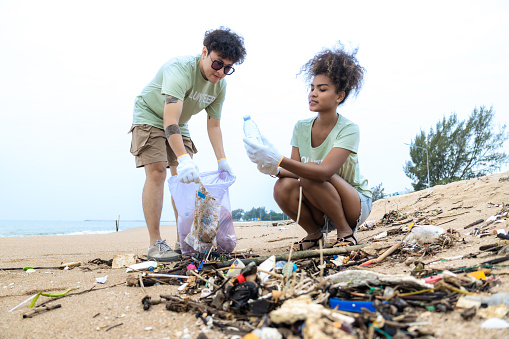 A beautiful African mid-adult woman and her LGBTQ Asian couple helping to pick up garbage on the beach during traveling on vacation. Social responsibility