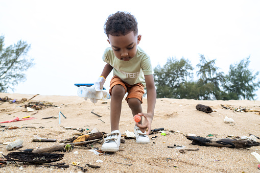 A 3-year cute African boy learning from his family to conserve our planet, picking up garbage on the beach during vacation. Social responsibility
