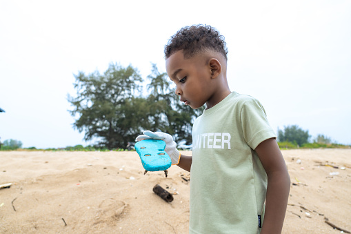 A 3-year cute African boy learning from his family to have responsibility to our planet, picking up garbage on the beach during vacation. Social responsibility