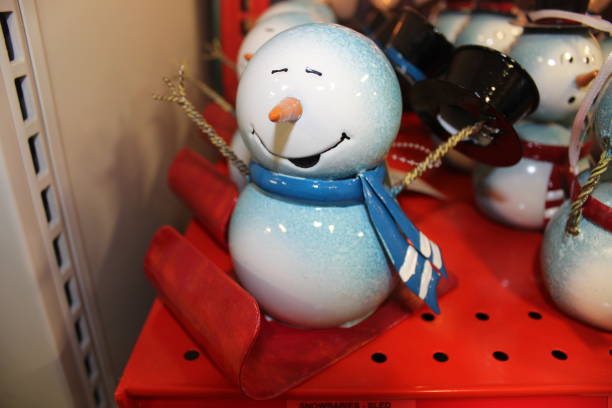 A snowman decoration that has its hands in the air riding a red sled.