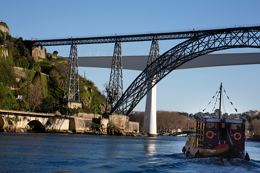 A tourist boat sails under the Dona Maria Pia bridge designed by Gustav Eiffel and in the background the Sao Joao bridge in O Porto and over the Douro River