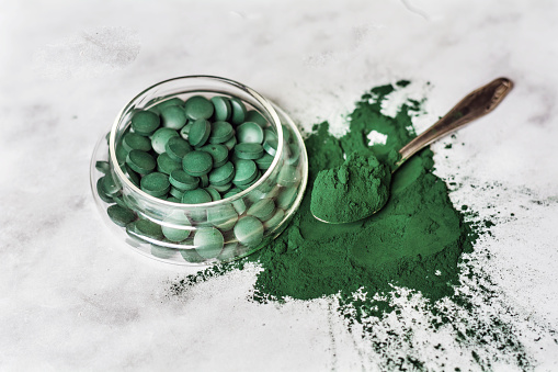 Green Spirulina tablets and powder in bowls