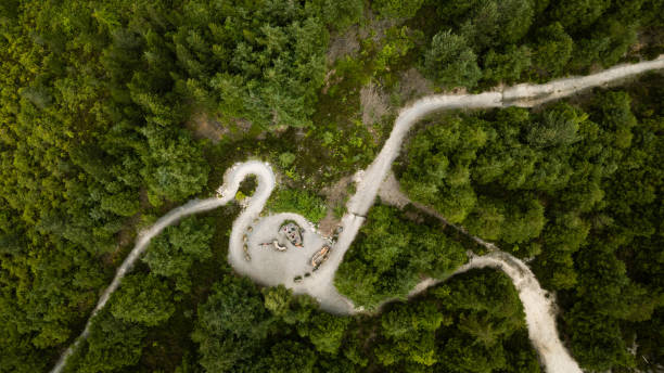 Overhead drone point-of-view shot of three female friends riding together on mountain bikes along a bike trail all wearing activewear and bike helmets. The forest is located in Hamsterley Forest in Durham, England.