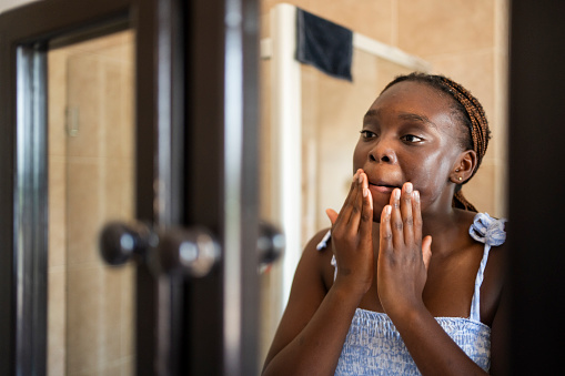 Teenage girl examining her complexion reflected in a bathroom mirror at home in the morning