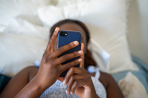 Close-up of a young teenage girl using a smart phone while lying alone on her bed at home