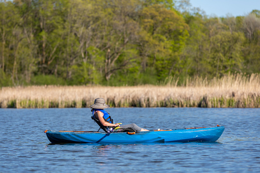 Side view of a young girl in her blue kayak on the lake. Taken on a beautiful springtime day in Minnesota, USA. In this image she has her hat over her face and is resting in her kayak.