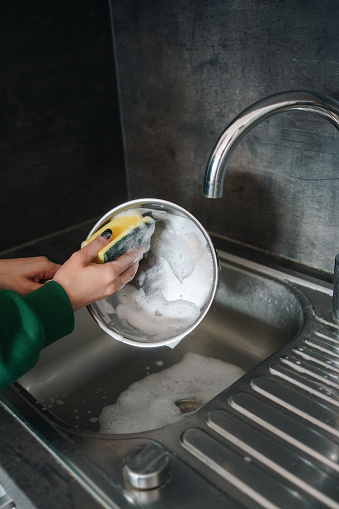 Woman washing a pan with a sponge in the kitchen