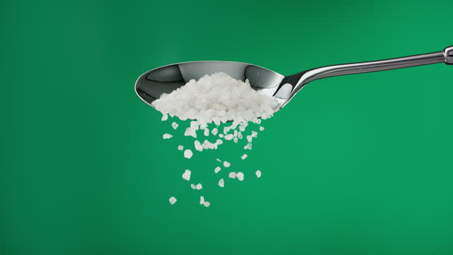 Super slow motion Himalayan white coarse-grained salt falling from a metal spoon