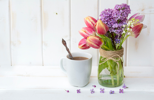 A cup of coffee on a white wooden background and  bouquet of lilac flowers