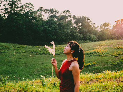 Asian woman blowing glass flower with sunlight in nature. Outdoors. Enjoy Nature. Healthy Smiling Girl on spring lawn. Allergy free concept. Freedom