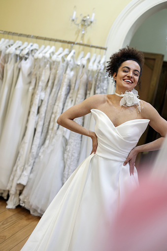 Young woman trying on a wedding dress in a bridal shop. About 25 years old, mixed-race brunette.