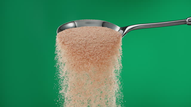 Super slow motion pile of brown ground sugar falling from a metal spoon