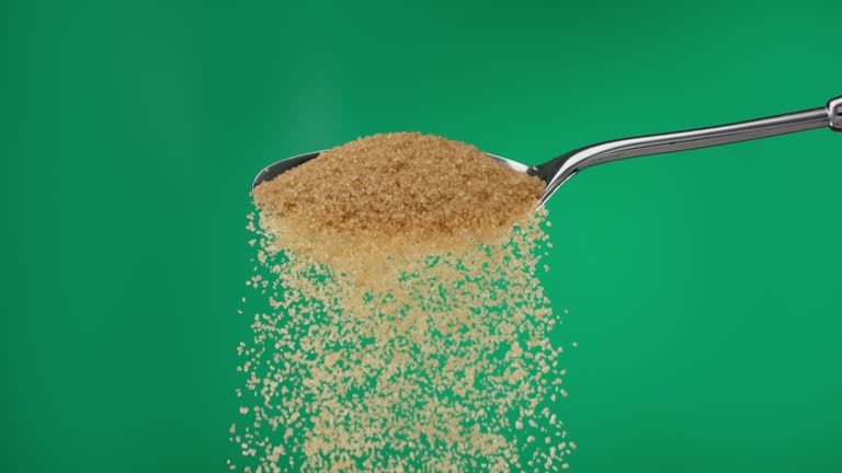 Super slow motion pile of brown ground sugar spilling from a metal spoon