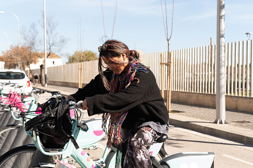 Side view portrait of a concentrated latin woman riding a bike from the public bike system