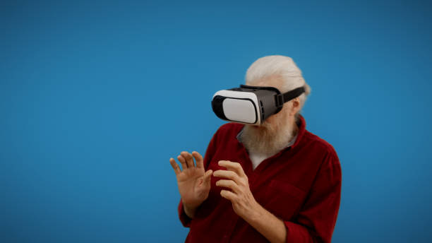 istock Mature man in VR glasses appears scared while trying futuristic technology, set against a blue background 1998267681