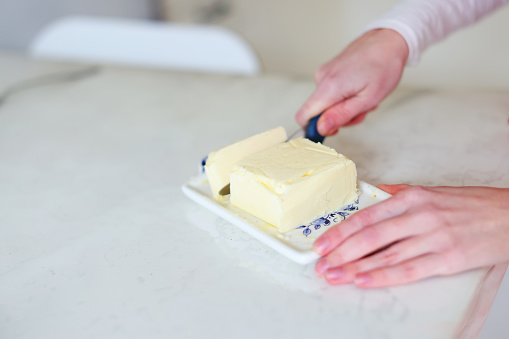 Woman cuts off butter for smearing aluminum foil before baking biscuit.