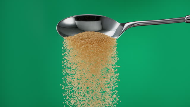 Super slow motion pile of brown sugar spilling from a metal spoon