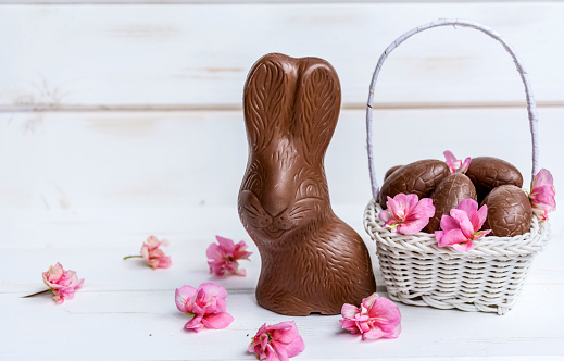 Chocolate Easter Bunny, Chocolate Eggs and Pink Flowers on a White Wooden Background .Easter Greeting Card