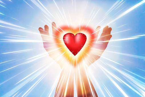 Raised hands holding a glowing red heart with beautiful light beams. Can illustrate the concept of love, harmony, spirituality, wellbeing, positive energy, etc.