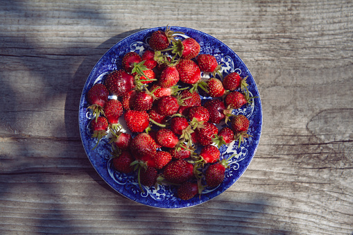 strawberries in wooden basket, standing on weathered wooden background, outdoors in summer, in the garden, elder blossom added