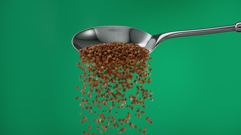 Super slow motion pile of raw brown buckwheat groats grain falling from a spoon