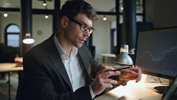 istock Finance broker working late in lamp light. Serious businessman check computer 1998400476
