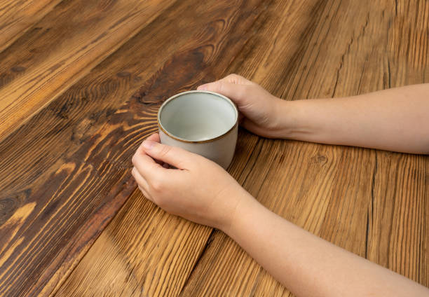 istock Hand Holds Cup, Empty Cup in Hands, Coffee Mug, Teacup Mockup, Cup in Arms on Wooden Table 1998435834