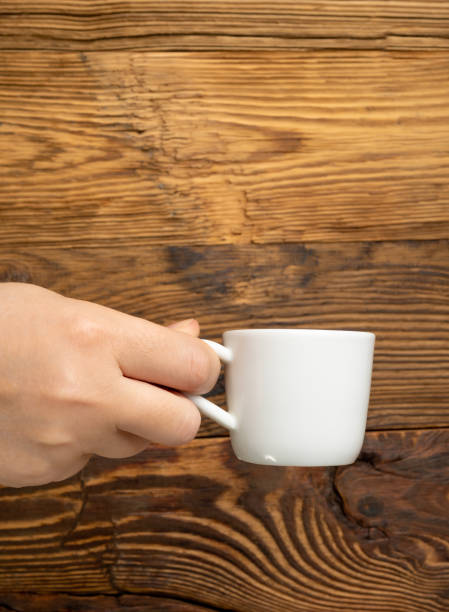 istock Hand Holds Cup, Empty White Cup in Hands, Coffee Mug, Teacup Mockup, Cup in Arms on Wooden Table 1998435842