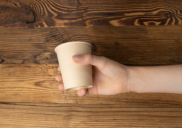 istock Hand Holds Cup, Empty Paper Cup in Hands, Coffee Mug, Teacup, Hot Beverage Mockup, Cup in Arms 1998435846