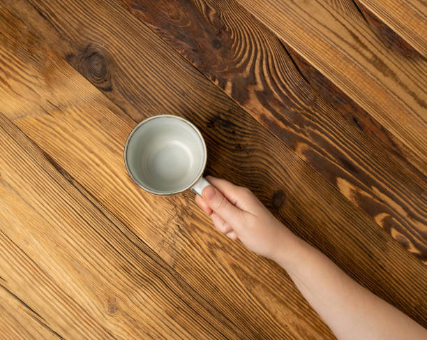 istock Hand Holds Cup, Empty Cup in Hands, Coffee Mug, Teacup Mockup, Cup in Arms on Wooden Table 1998435847