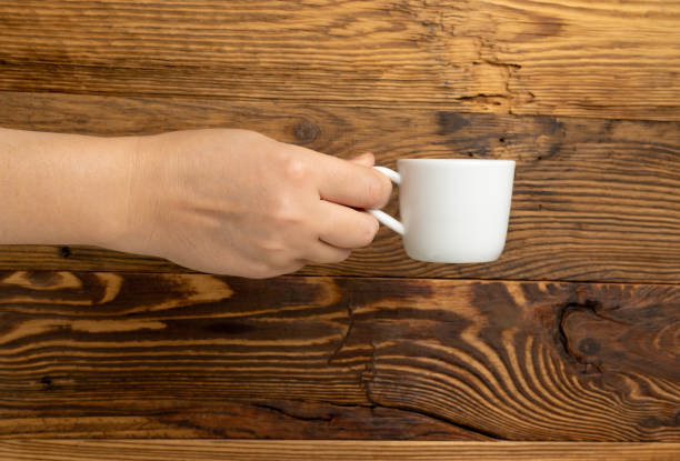 istock Hand Holds Cup, Empty White Cup in Hands, Coffee Mug, Teacup Mockup, Cup in Arms on Wooden Table 1998435853