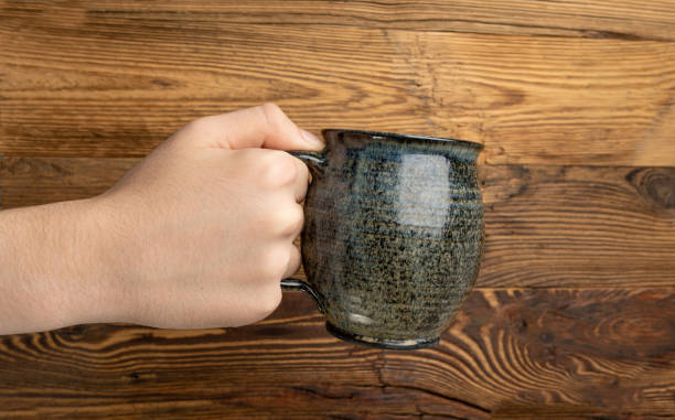 istock Hand Holds Cup, Empty Cup in Hands, Coffee Mug, Teacup Mockup, Cup in Arms on Wooden Table 1998435875