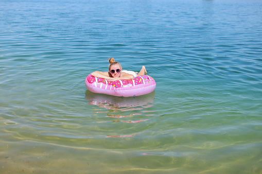 Beautiful young woman with inflatable donut ring relaxing in sea