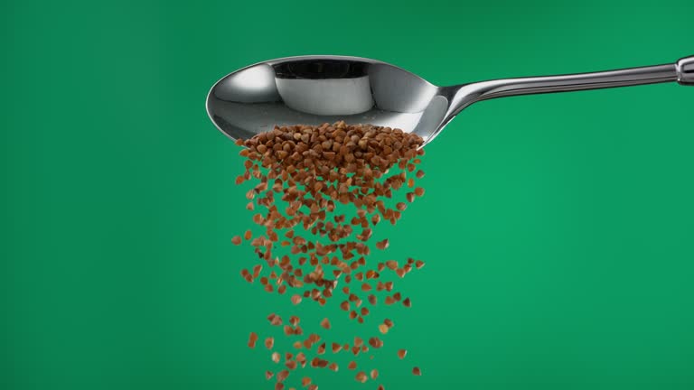 Super slow motion pile of brown buckwheat groats grain spilling from a spoon