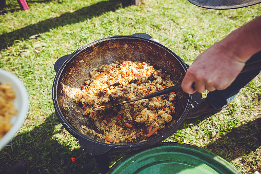 A large black cooking pot with Uzbek pilaf on green grass background. The pilaf is made with rice, meat, carrots, onions, and spices, and its a traditional dish in Central Asian cuisine.