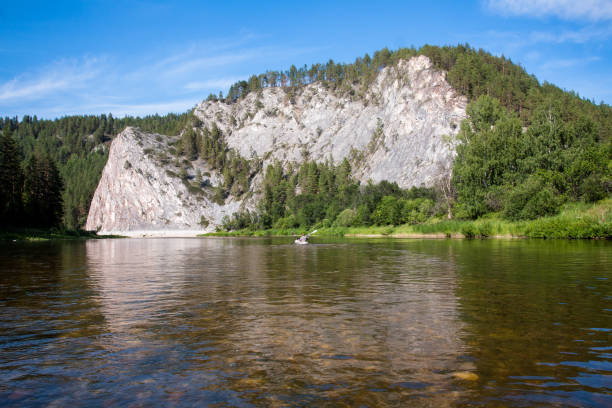 istock Tranquil River Scene with Rocky Cliff, Lush Green Trees, and Serene Blue Sky 1998448444